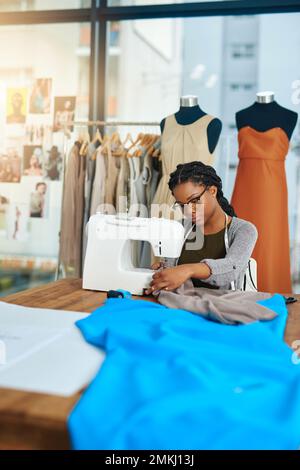 Nähen ist meine Superkraft. Eine junge Modedesignerin, die in ihrer Werkstatt eine Nähmaschine benutzt. Stockfoto