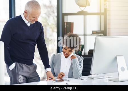 Ich verwende diese App, um die Märkte zu verfolgen. Ein reifer Geschäftsmann, der seinem Kollegen etwas auf einem Tablet zeigt. Stockfoto