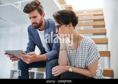 Unternehmer tun, was sie am besten können. Zwei junge Kreative, die auf einem digitalen Tablet in einem modernen Büro zusammenarbeiten. Stockfoto