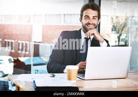 Ich werde den Job erledigen. Freigestelltes Porträt eines gutaussehenden jungen Geschäftsmanns, der im Büro an seinem Laptop arbeitet. Stockfoto