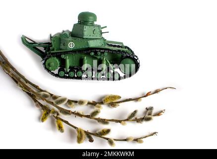 Modell eines alten sowjetischen Panzers aus Papier auf weißem Hintergrund. Weidenzweig im Vordergrund. Seitenansicht. Das Konzept der Handarbeit. Stockfoto