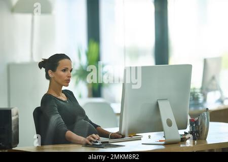 Ich kümmere mich im dritten Trimester ums Geschäft. Eine schwangere Geschäftsfrau, die in einem Büro arbeitet. Stockfoto