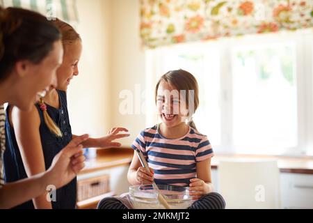 Mom und ihre kleinen Bäcker. Zwei kleine Mädchen, die mit ihrer Mutter in der Küche backen. Stockfoto