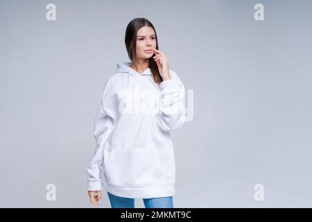 Junges Hipster-Mädchen in weißem Baumwollpullover mit Bereich für Ihr Logo, weiße Damen Modell, helle Wand im Hintergrund mit Kopierbereich für Ihr Design oder im Studio aufgenommene Inhalte Stockfoto