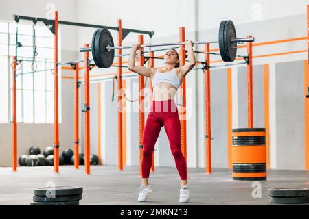 Ganzkörper-kräftige Gewichtheberin in Leggings und BH für Frauen, die beim täglichen Training im Fitnessstudio Pressübungen mit einer schweren Klingel durchführen Stockfoto