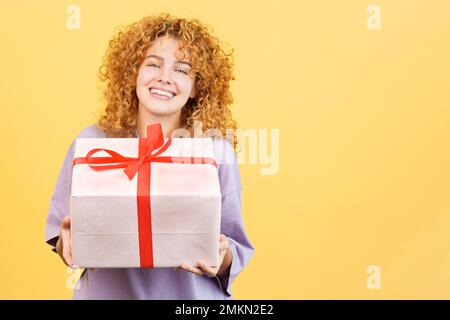 Glückliche Frau, die vor der Kamera lächelt, während sie ein Geschenk überreicht Stockfoto