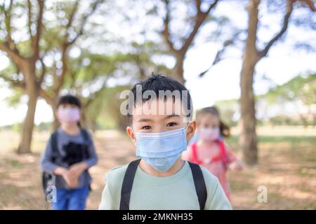 Junge und Mädchen gehen nach Covid-19-Quarantäne und Abriegelung wieder zur Schule. Gruppe von Kindern in Masken zur Coronavirus-Prävention. Stockfoto