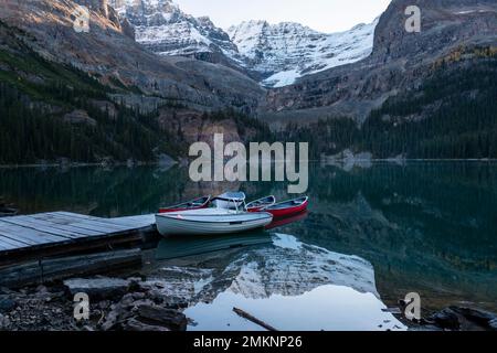 Berge und Boote spiegeln sich im klaren Wasser des Lake O'Hara, des Yoho-Nationalparks und der Kanadischen Rocky Mountains wider. Stockfoto