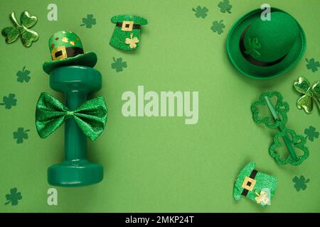 Gym-Kurzhantel, grüne irische Hüte mit Blätterklee und Gläsern in Shamrock-Form. Fitness-Workout flach liegend für St. Patrick's Day, mit Kopierraum. Stockfoto