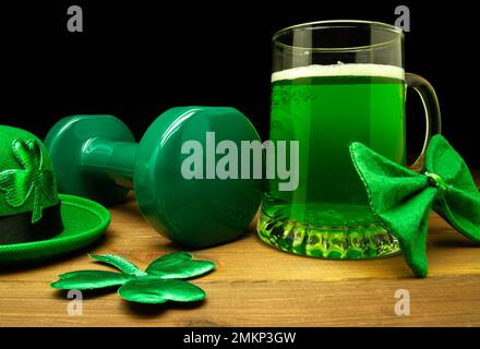 Kurzhantel, ein Glas grünes Bier, irischer Hut mit Shamrock-Klee. St. Patrick's Day Fitness-Komposition. Fitnessstudio und Sporttrainingskonzept. Stockfoto