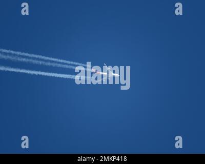 Blick auf ein Flugzeug mit rot-weißer Lackierung, das in großer Höhe mit Kondensstreifen fliegt Stockfoto