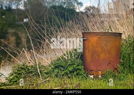 Rostiger alter Abfalleimer für Gartenabfälle im langen Gras am Flussufer Stockfoto