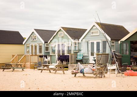 DORSET, Großbritannien - 07. Juli 2022. Ein Mann im Urlaub, der sich vor einer Reihe von Holzhütten am Strand erholt, Hengistbury Head, Dorset, Großbritannien Stockfoto