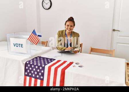 Junge schöne hispanische Frau Wahltisch Präsident schriftlich auf Zwischenablage an Wahlhochschule Stockfoto