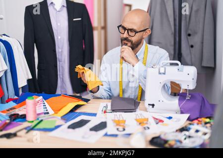 Ein junger kahlköpfiger Schneider, der Stoff in der Schneiderei hält Stockfoto
