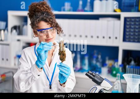 Junge hispanische Wissenschaftlerin hält Marihuana-Pflanze mit Pinzette im Labor Stockfoto