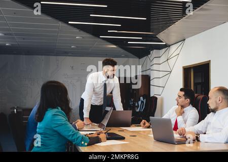 Silhouetten von Menschen, die am Tisch sitzen. Team junger Geschäftsleute, die in einem modernen Büro zusammenarbeiten und miteinander kommunizieren. Unternehmensteam und Stockfoto