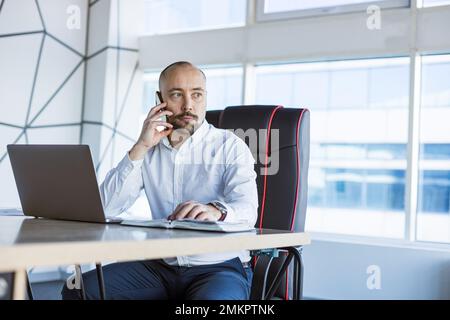 Porträt eines betriebsjungen, erfolgreichen Mannes in einem modernen Büro am Tisch Stockfoto