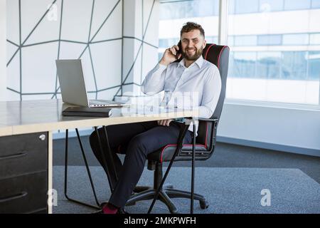 Porträt eines betriebsjungen, erfolgreichen Mannes in einem modernen Büro am Tisch Stockfoto