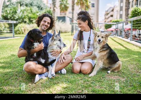 Mann und Frau Paar lächeln selbstbewusst auf Kraut mit Hunden im Park sitzen Stockfoto
