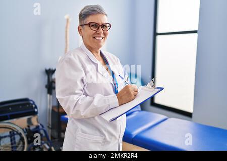Frau im mittleren Alter, Physiotherapeutin, die in der Reha-Klinik auf die Zwischenablage schreibt Stockfoto