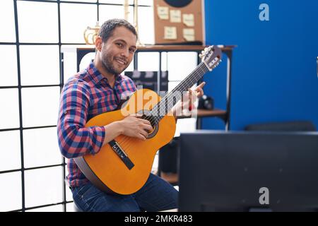 Junger Musiker, der im Musikstudio lächelnd und selbstbewusst klassische Gitarre spielt Stockfoto