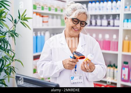 Grauhaarige Frau im mittleren Alter, Apothekerin, die in der Apotheke eine Tablettenflasche scannt Stockfoto