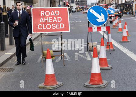 Ein Geschäftsmann navigiert selbst durch Verkehrskegel bei einer Straßensperrung im Zentrum von London, England, Großbritannien Stockfoto