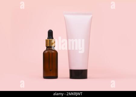 Modellflasche mit rosafarbener Quetschflasche, Kunststoffröhrchen mit schwarzem Verschluss und brauner Glasflasche mit Pipette auf rosa Hintergrund. Vorderansicht, Kopierbereich. Cosme Stockfoto