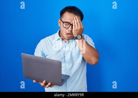 Chinesischer junger Mann, der einen Computer-Laptop benutzt und müde gähnt und mit der Hand Gesicht, Augen und Mund bedeckt. Das Gesicht tut weh. Stockfoto