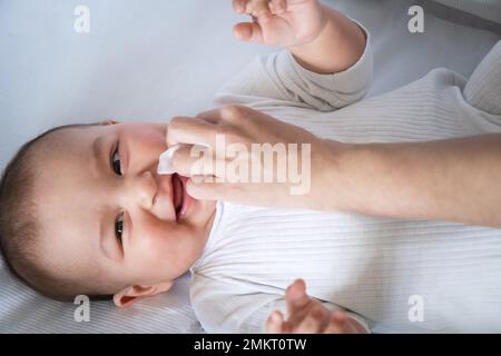 Mom wischt den Sabber des Babys mit einer Serviette ab. Babypflege, Zahnen, Sabbern. Stockfoto