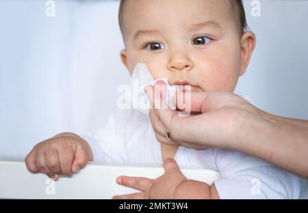 Mom wischt den Sabber des Babys mit einer Serviette ab. Babypflege, Zahnen, Sabbern. Stockfoto