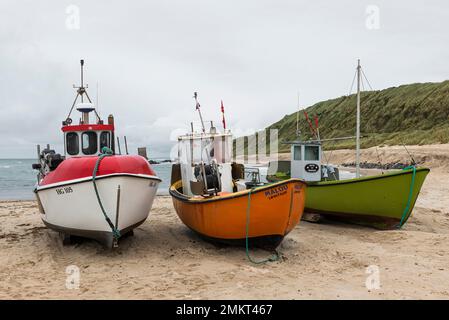 Dänemark, Nordjütland, Lönstrup: Drei farbenfrohe Fischerboote, die am Sandstrand unter einem bedeckten Himmel gezogen wurden. Stockfoto