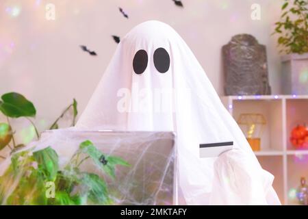 Ghost of Halloween nutzt Laptop im Internet surfen, Online-Shops durchsuchen, Märkte. Ein Geist macht eine Bestellung vom Computer für Halloween. Ghost zahlt für den Online-Kauf per Kreditkarte. Stockfoto