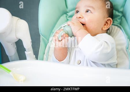 Ein glückliches und zufriedenes Baby isst Bananenpüree von einem Nippel. Einführung von Ergänzungsnahrung, gesunder Babynahrung, Ernährung des Babys am Tisch Stockfoto