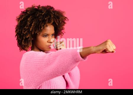 Ernsthaft zuversichtlich, junge, schwarze, geschwungene Frau, die auf pinkfarbenem Hintergrund mit der Hand zuschlägt, Nahaufnahme Stockfoto