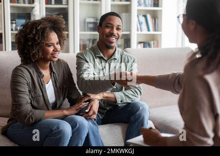 Glückliches afrikanisches Paar schüttelt die Hand des Familienberaters, erfolgreiche Ehetherapie Stockfoto