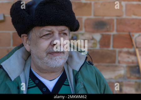 Außenporträt eines bärtigen ukrainischen Bauern, der mit Hoffnung blickte, während er mit Kürbis in den Händen stand und ihn anschaute, während er gegen B saß Stockfoto