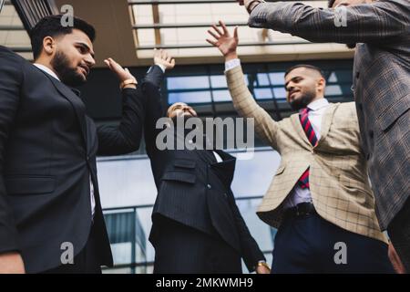 Internationales Business-Team von erfolgreichen Menschen, die den Sieg feiern. Männer in Anzügen freuen sich bei einer Unternehmensversammlung über die Leistungen ihres Unternehmens Stockfoto