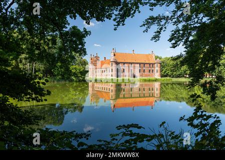 Dänemark, Jütland, Djursland: Die Renaissancefassade des Schlosses Rosenholm spiegelt sich im Wasser wider und wird von Blättern und Zweigen eingerahmt Stockfoto