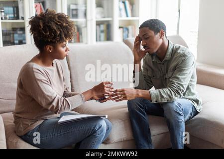 Afrikanische Psychotherapeutin gibt männlichen Patienten ein Glas Wasser Stockfoto
