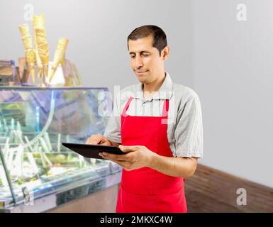 Ein lächelnder Mitarbeiter im Eiscafé steht hinter der Theke im Geschäft und verwendet ein digitales Tablet Stockfoto