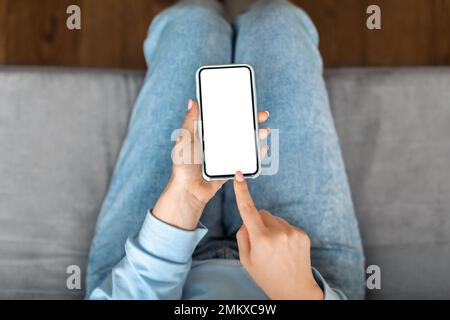 Nicht Wiedererkennbare Junge Frau, Die Zu Hause Ein Smartphone Mit Leerem Weißen Bildschirm Verwendet Stockfoto