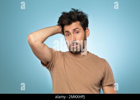 Frustrierter, befragter, bärtiger Mann, der Hand an Kopf legt, auf blauem Hintergrund steht, Studioaufnahme Stockfoto