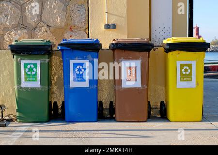 Vier farbige Mülltonnen in einer Reihe gegen ein Gebäude. Alle mit universellen Recycling-Symbolen gekennzeichnet. Spanische Wörter. Schwarze Räder. Müllsäcke. Stein Stockfoto