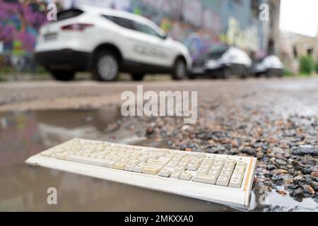 Alte, kaputte Computertastatur, in den Müll geworfen, auf der Straße in einer Pfütze gelegen Stockfoto