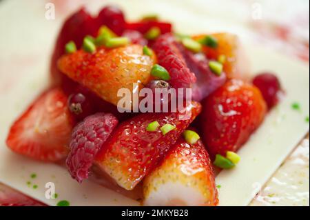Nahaufnahme von Erdbeeren, Himbeeren und roten Johannisbeeren auf einem Käsekuchen mit weißer Schokolade und zerdrückten Pistazien. Hintergrund für Kuchendessert. Stockfoto