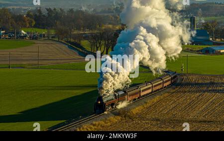 Drohne Blick auf eine antike Dampfmaschine, Annäherung, Dampfblasen und Reisen entlang der Landschaft an einem sonnigen Tag Stockfoto