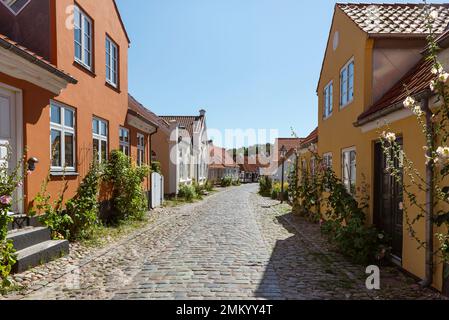 Dänemark, Jütland, Djursland, Ebeltoft: Farbenfrohe Fassaden und Klippen in den Gassen der Altstadt in der Sonne vor blauem Himmel Stockfoto