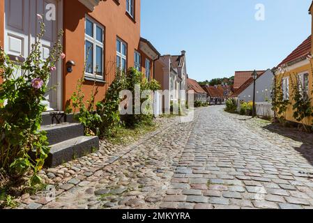 Dänemark, Jütland, Djursland, Ebeltoft: Farbenfrohe Fassaden und Klippen in den Gassen der Altstadt in der Sonne vor blauem Himmel Stockfoto